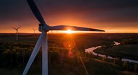 Wind turbine at sunset with golden light streaming through blades over rural landscape with winding river and forest creating dramatic renewable energy scene.