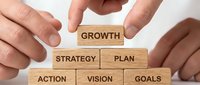 Hands arranging wooden blocks in pyramid shape with business words: growth, strategy, plan, action, vision, goals. Corporate success concept.