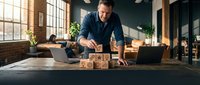 Middle-aged Caucasian male entrepreneur arranging wooden blocks on desk in modern office with laptop, symbolizing business growth, strategy planning and success in startup environment.