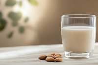 Fresh glass of almond milk with raw almonds on natural linen tablecloth against blurred green background, healthy dairy alternative beverage.