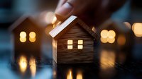 Glowing wooden house silhouette with warm window lights against blurred bokeh background creates cozy evening atmosphere, symbolizing home comfort and tranquility.
