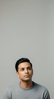 Young man with dark hair and South Asian ethnicity wearing gray crew neck shirt, looking upward against neutral gray background, isolated portrait for commercial and editorial use.