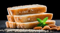 Sliced fresh bread with sesame seeds and almonds on dark stone background with basil leaf garnish, dramatic lighting creates appetizing mood for food photography.