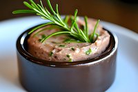 Fresh salmon mousse garnished with rosemary sprig served in dark ceramic ramekin. Creamy pink appetizer with herbs and spices for gourmet dining experience.