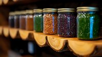 Glass jars filled with colorful grains, seeds and spices arranged on rustic wooden shelves, creating pantry storage display with natural food ingredients.