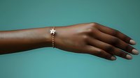 Female African American arm wearing delicate gold bracelet with star charm against turquoise background, showcasing elegant jewelry and minimalist fashion styling.