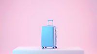 Light blue travel suitcase on a white podium against a soft pink background, evoking summer vacation, tourism, and modern travel lifestyle.