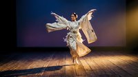 Young Asian woman in flowing white dress performing contemporary dance on wooden stage floor with dramatic purple lighting and motion blur effects.
