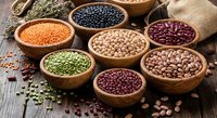 Assorted legumes and grains in wooden bowls on rustic table. Healthy protein sources including lentils, beans, chickpeas for cooking and nutrition.