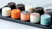 Modern individual mousse desserts in various colors and flavors arranged on black rectangular plate, elegant pastry presentation for restaurant or catering service.