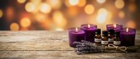 Purple candles with essential oil bottles and dried lavender on rustic wooden table against warm bokeh background for aromatherapy and spa relaxation.