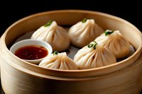 Steamed dumplings in traditional bamboo basket with spicy dipping sauce, garnished with fresh herbs, close up view of Asian dim sum cuisine.