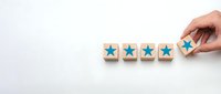 Hand placing wooden blocks with blue stars for customer rating and feedback evaluation on white background for business quality assessment.