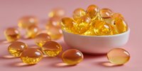 Golden omega-3 fish oil capsules in white bowl and scattered on pink background, showcasing nutritional supplements for health and wellness.
