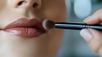 Close up of makeup artist applying lipstick with professional brush on young caucasian woman lips. Beauty and cosmetics concept for social media and advertising.