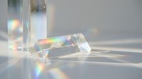Crystal prism refracting light into rainbow spectrum on neutral surface, creating optical effects and prismatic shadows for scientific and design applications.
