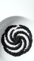 Black sesame seeds arranged in a spiral pattern on a white ceramic plate, overhead view. Use for food styling, nutrition, cooking, and culinary design projects.