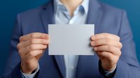 Business professional in navy blue suit holding blank white card at chest level, presenting empty mockup space for text or design against blurred background.