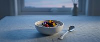 Colorful breakfast cereal bowl with berries and milk on blue table by window with morning light and ocean view.