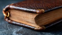 Vintage leather bound book with aged yellow pages and worn brown cover photographed in dramatic lighting against dark background, showing texture and detail.