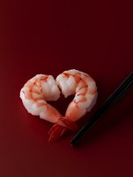 Fresh cooked shrimp arranged in heart shape with black chopsticks on deep red background, romantic seafood concept for Valentine's day or date night dining.