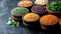 Colorful variety of raw legumes and pulses in wooden bowls on dark background. Fresh herbs add natural accent to healthy protein sources and superfoods.