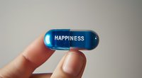 Fingers holding blue transparent pill capsule with happiness text against neutral background, conceptual healthcare and mental wellbeing metaphor.