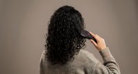 Young woman with curly dark hair brushing her natural textured locks from behind, wearing cozy sweater against neutral background for haircare concepts.