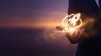 Businessman holding glowing rocket icon in palm against purple sunset sky representing startup launch, innovation, business growth and entrepreneurship success.