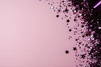Black star-shaped confetti scattered on pink background with diagonal composition and negative space for text, creating festive celebratory mood.