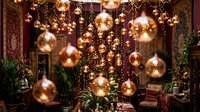 Luxurious restaurant interior with golden Christmas ornaments hanging from ceiling, creating festive holiday dining atmosphere with warm lighting and elegant decor.