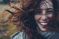 Young woman with flowing red hair laughing joyfully on windy autumn day, wearing gray scarf. Natural candid moment captures genuine happiness and carefree spirit.