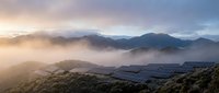 Solar panel farm in mountainous landscape at sunrise with dramatic mist and golden light creating sustainable energy concept for renewable power generation.