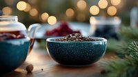 Aromatic cocoa powder in turquoise ceramic bowl against blurred festive lights background, cozy winter atmosphere with spices and holiday decorations.