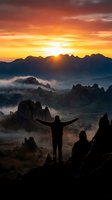Silhouette of a man standing on a rocky mountain peak with arms raised wide, facing a dramatic golden sunset over misty mountain valleys.