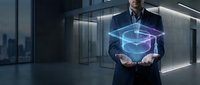Professional businessman in dark suit presenting glowing blue holographic cube technology in modern office environment for digital innovation concepts.