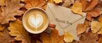 Autumn flat lay with latte art coffee cup and thank you envelope on golden fall leaves, cozy seasonal greeting concept.