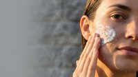 Young woman applying facial scrub exfoliant on cheek for skincare routine and natural beauty treatment outdoors.