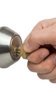 Hand inserting brass key into modern cylindrical door lock on white background for home security and locksmith services.