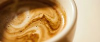 Creamy coffee with latte art foam swirl in white cup, close-up of hot beverage for café, restaurant, and coffee shop marketing materials.