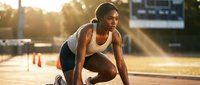 Young Black female athlete in starting position on track, focused and determined, golden hour sunlight, sports and fitness concept.