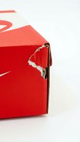 Damaged red cardboard shipping box with torn corner showing wear from delivery and handling on white background for packaging concepts.