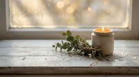 Cozy home interior with burning candle and eucalyptus branch on wooden windowsill creating warm atmospheric lighting for relaxation and wellness concepts.