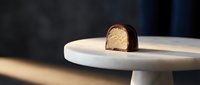 Chocolate-covered cake ball with golden sponge interior displayed on white plate, showcasing dessert plating and confectionery artistry for bakery and culinary content.
