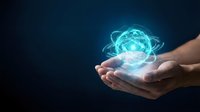 Hands holding glowing atom symbol with orbiting electrons on dark background, representing science, technology, innovation, and nuclear energy concepts for educational and business use.