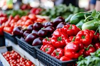 Fresh red bell peppers and purple eggplants displayed in black crates at farmers market. Organic vegetables showcase healthy eating and local produce shopping.