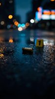 Crime scene investigation with bullet casing and evidence marker on wet asphalt at night with police lights and urban bokeh background for forensic concepts.