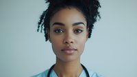 Young African American woman with natural curly hair and minimal makeup looking directly at camera against light blue background, professional headshot style portrait.
