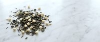 Dried herb mixture and tea leaves scattered on white marble surface for culinary and beverage preparation.