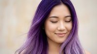 Young Asian woman with vibrant purple hair and closed eyes showing peaceful expression against soft neutral background for beauty and wellness content.